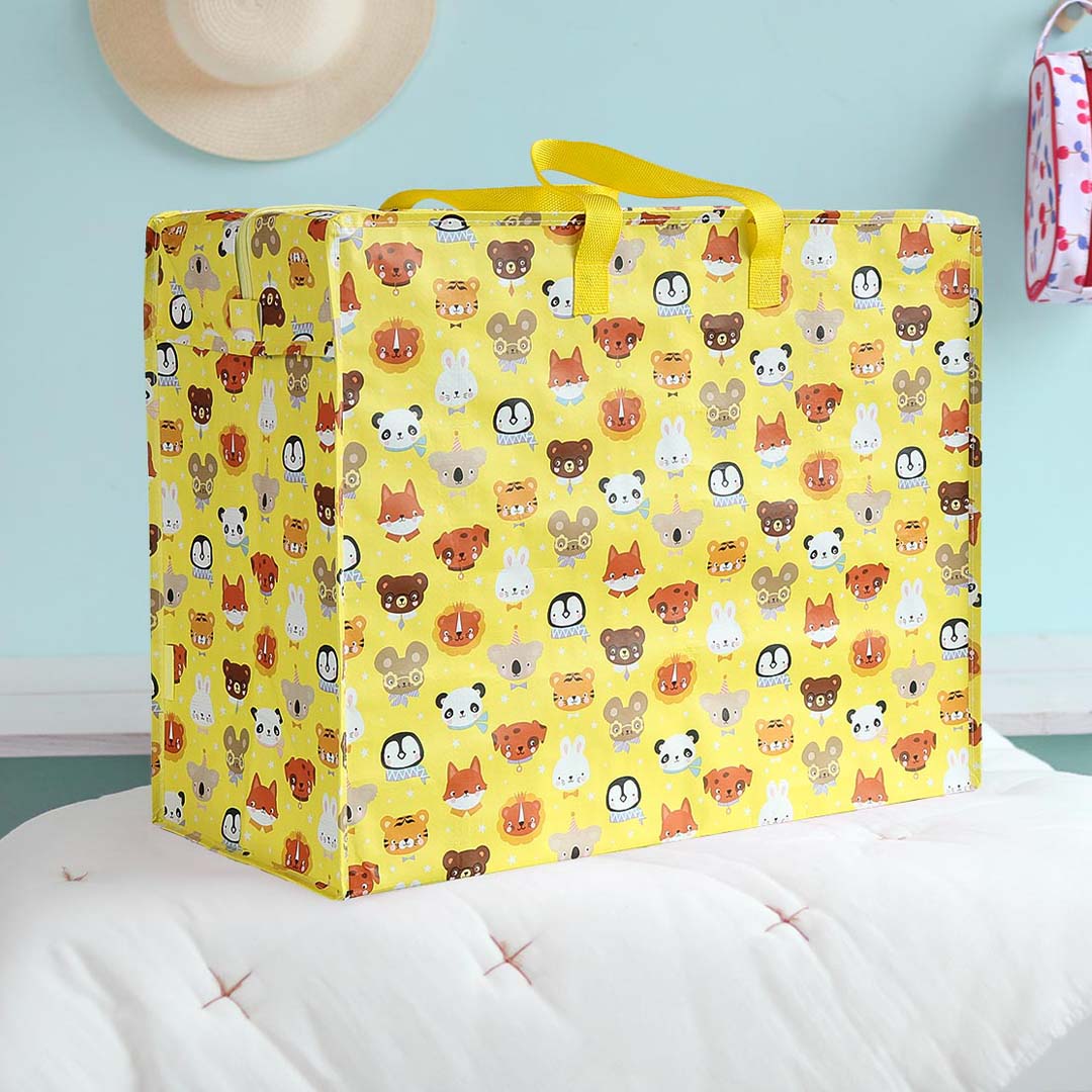 De a little lovely company opbergtas dierenvriendjes, een gele plastic opbergtas met een patroon van diverse dierenhoofden, staat op een wit bed in een kinderkamer.