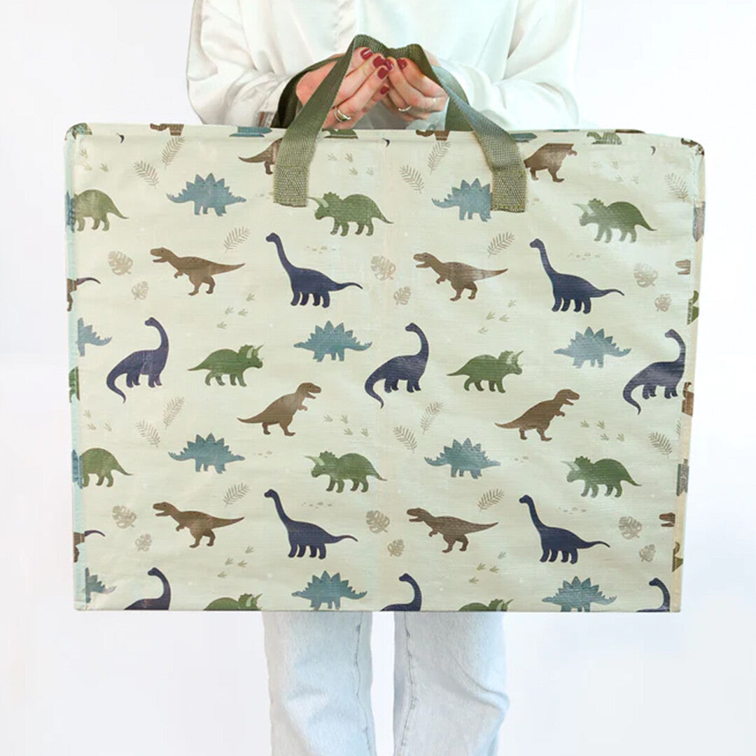 Een persoon houdt de A little lovely company beige opbergzak met dinosauruspatroon vast.