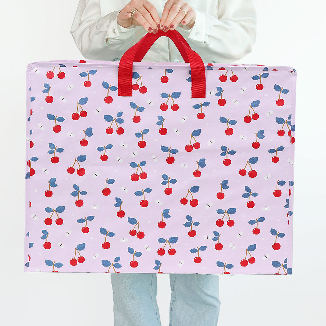 Een persoon houdt de a little lovely company roze opbergtas met kersenpatroon vast.