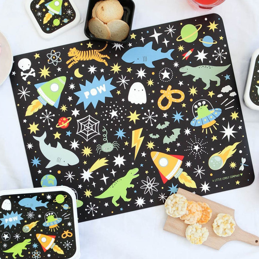 Een A Little Lovely Company placemat met galaxy patroon, omringd door bijpassende lunchboxen en snacks.