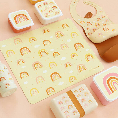 A little lovely company placemat met regenbogen en sterren, omringd door bijpassende lunchboxen, een drinkfles en een slab.