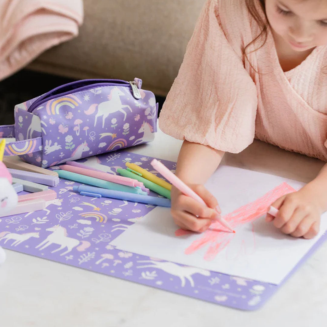 Een kind tekent op papier dat op de paarse eenhoorn placemat van a little lovely company ligt, met een bijpassend etui ernaast.