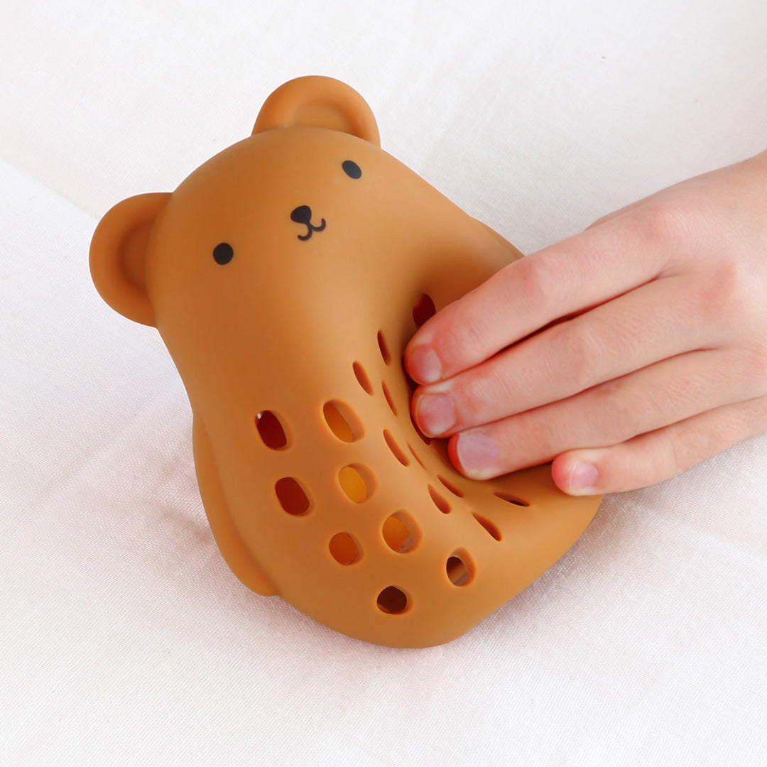 Een hand knijpt in de a little lovely company bruine siliconen berenrammelaar met gaten.