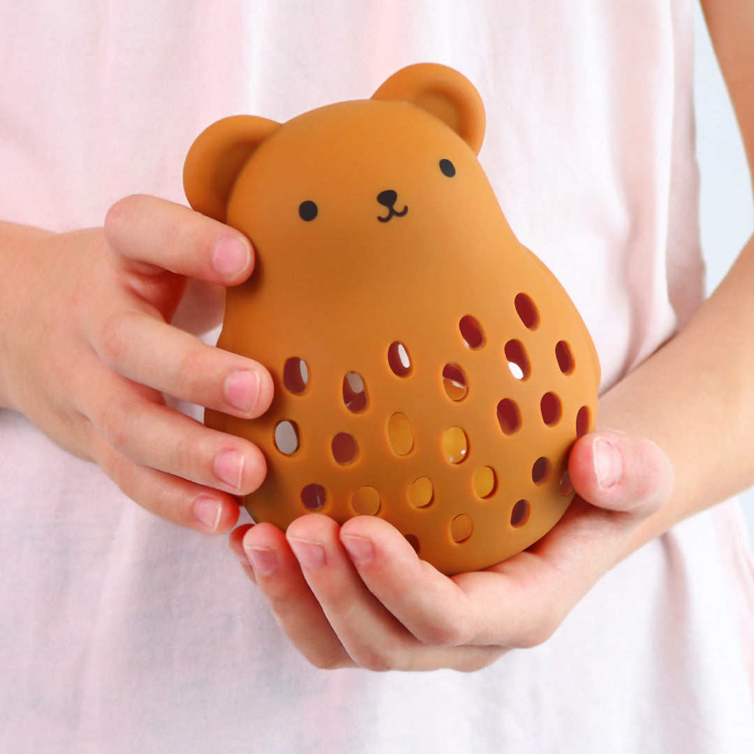 Kinderhanden houden de a little lovely company bruine siliconen berenrammelaar met gaten vast.