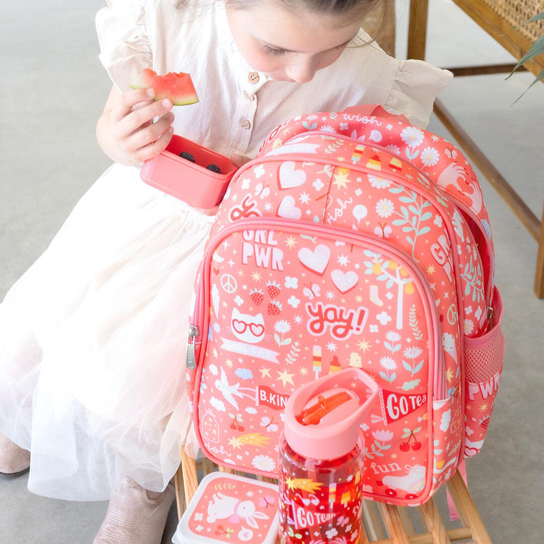 Een kind eet watermeloen naast de a little lovely company roze schoolrugzak met 'fun' patroon en een waterfles.
