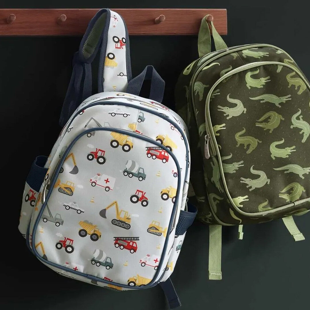 Twee schoolrugzakken hangen aan haken, links de a little lovely company rugzak met voertuigen en rechts een groene rugzak met krokodillen.