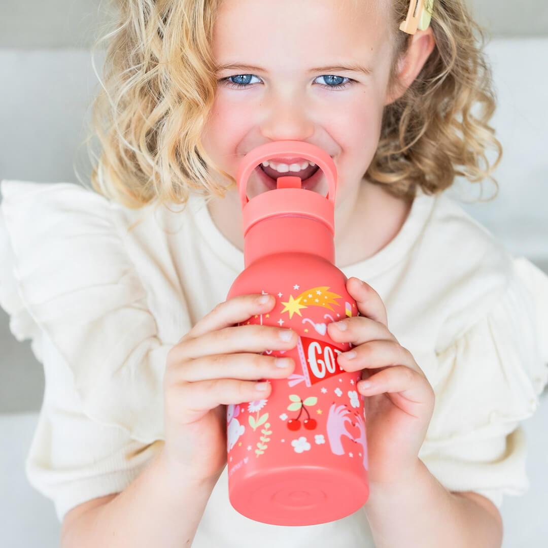 Een lachend kind drinkt uit de roze a little lovely company kinderdrinkfles met illustraties van kersen en een eenhoorn.