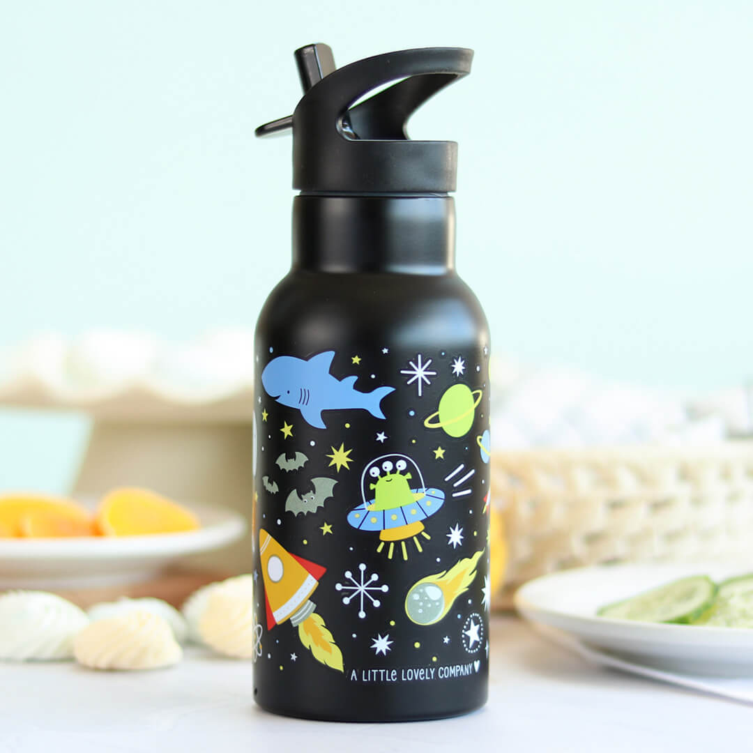 A Little Lovely Company zwarte kinder drinkfles met galaxy en ruimtefiguren op een tafel met eten.