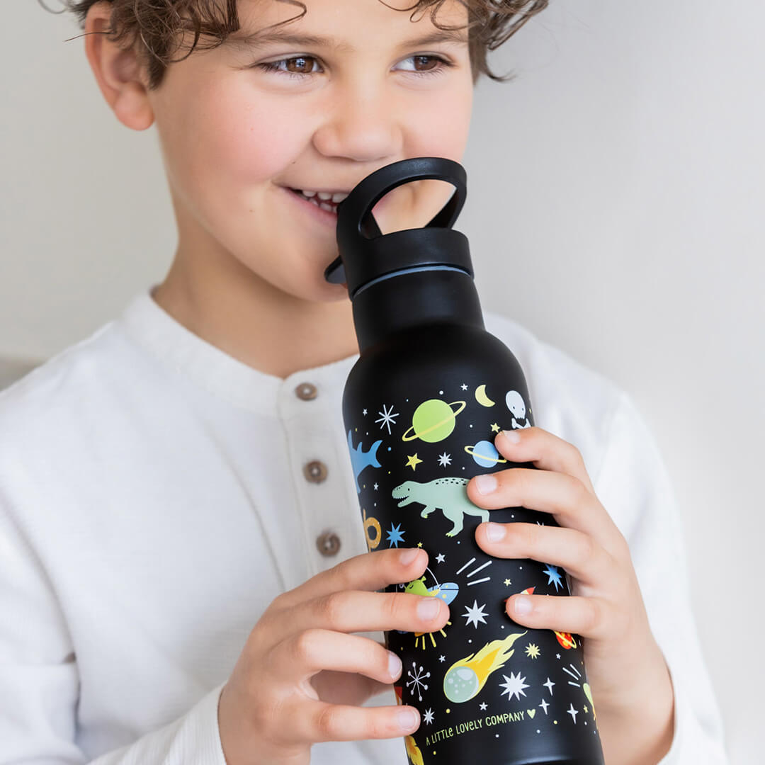 Een lachend kind drinkt uit de A little lovely company zwarte kinder drinkfles met galaxy-thema.