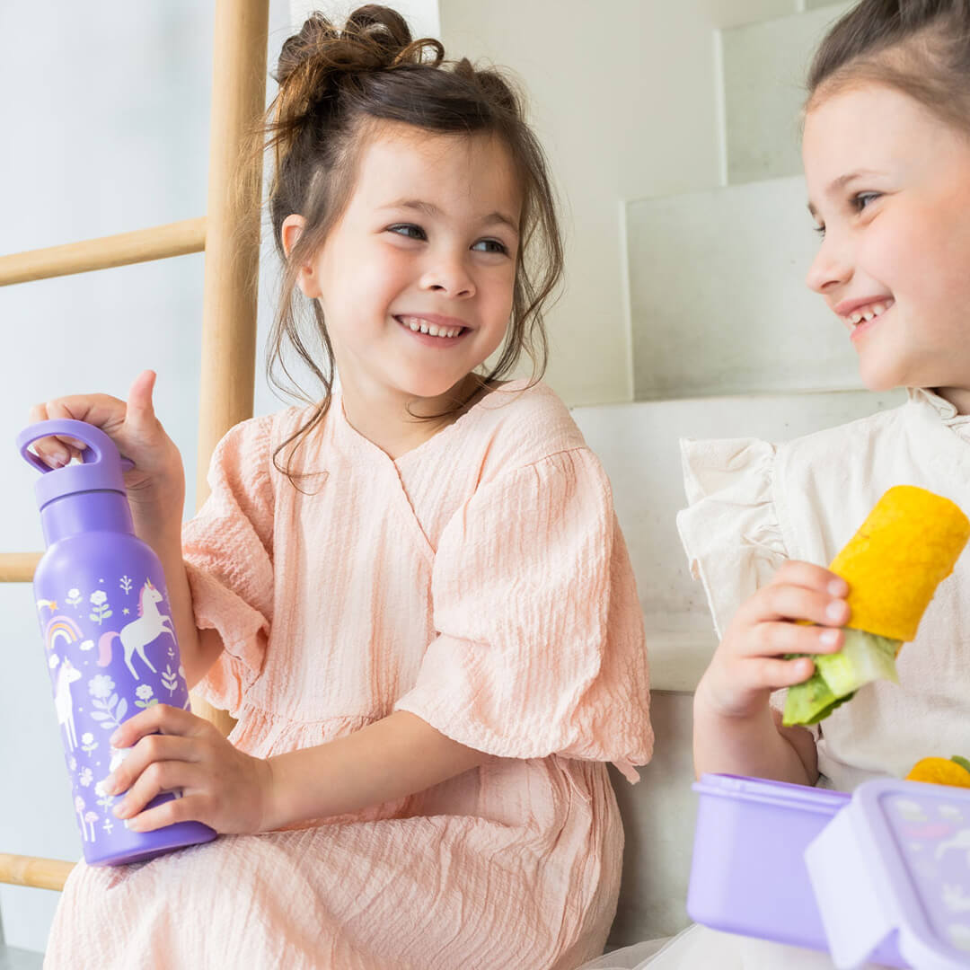 Twee lachende kinderen zitten op een trap, waarvan één een A Little Lovely Company paarse drinkfles met eenhoornpatroon vasthoudt.
