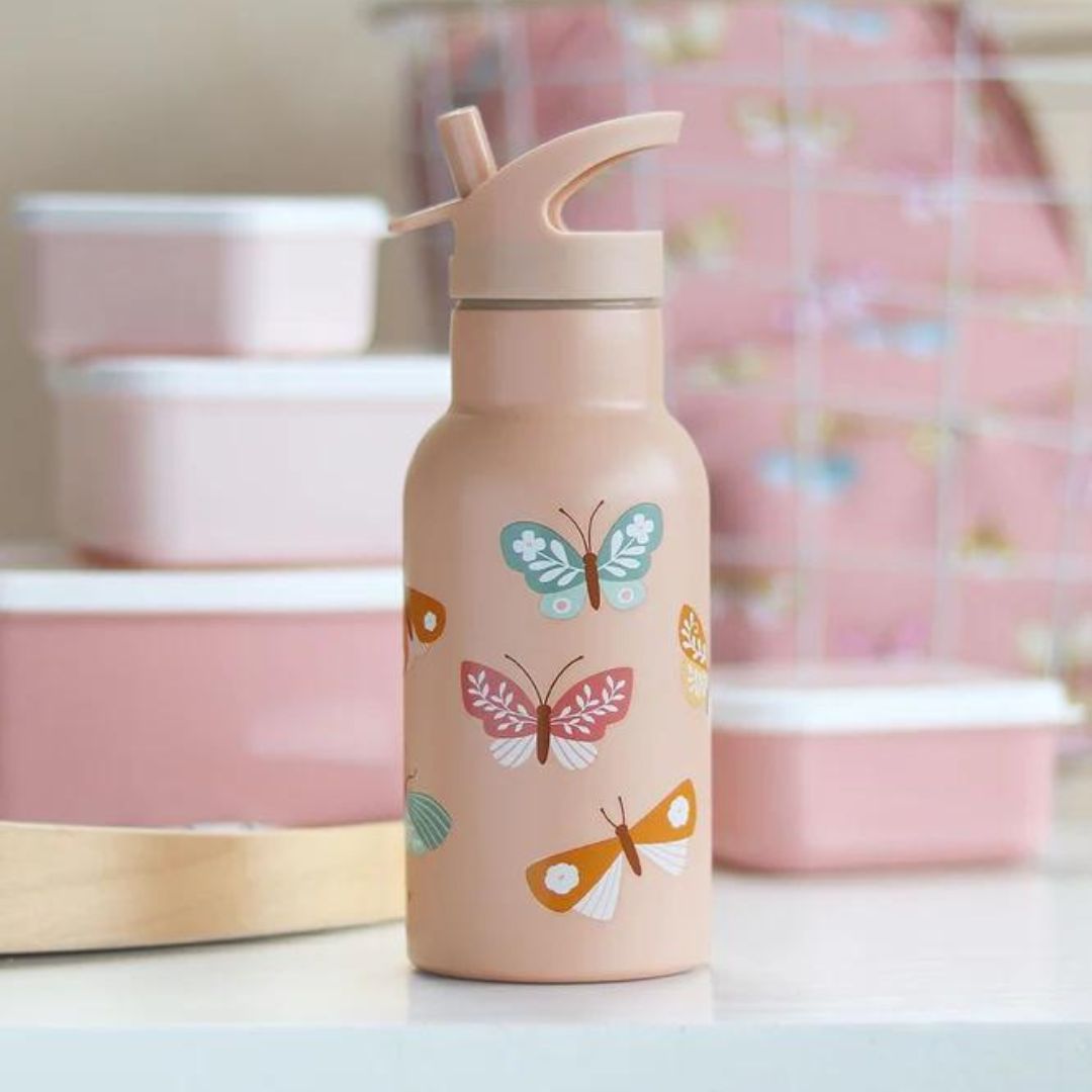 Roze kinderdrinkfles met vlinderprint en rietje, staand op een tafel met roze lunchboxen op de achtergrond.
