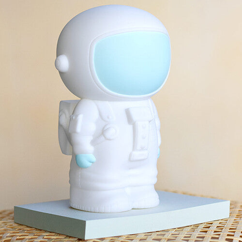Witte astronaut spaarpot van de zijkant gezien, staand op een lichtblauw blokje.