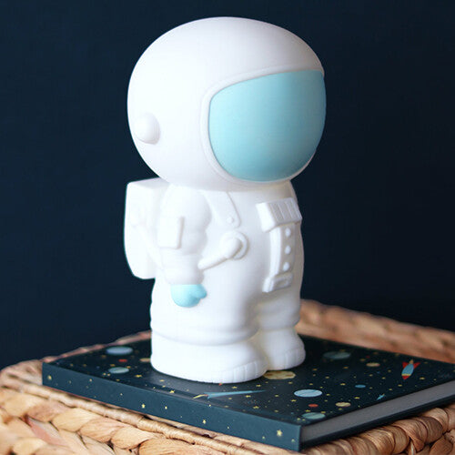 Witte astronaut spaarpot schuin van voren gezien, staand op een donkerblauw boek.