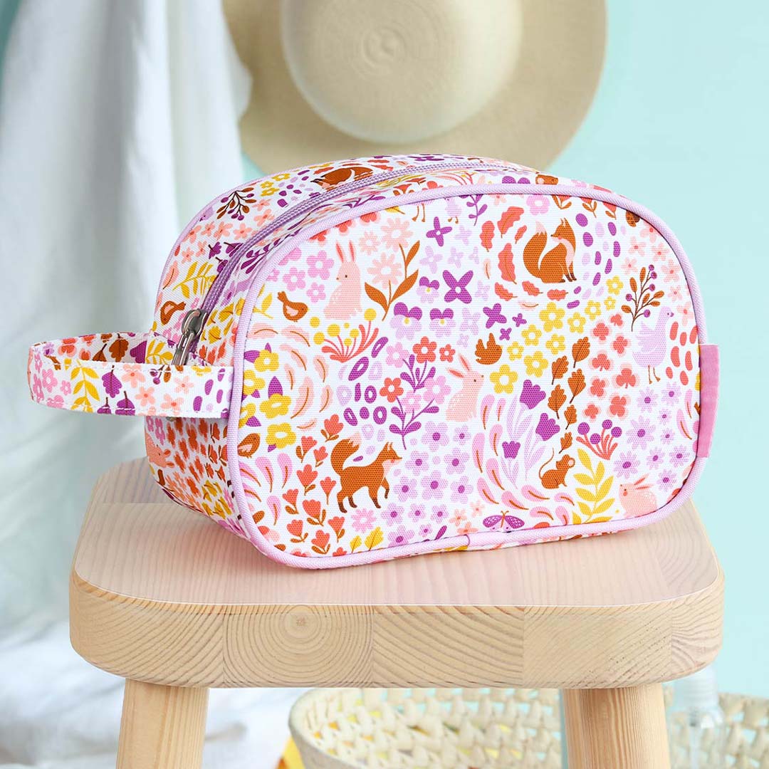 De a little lovely company toilettas met bloemen- en dierenprint staat op een houten krukje.