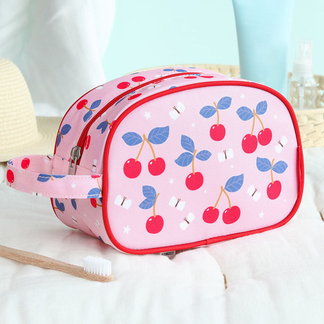 De a little lovely company roze toilettas met kersenpatroon staat op een witte handdoek naast een tandenborstel.