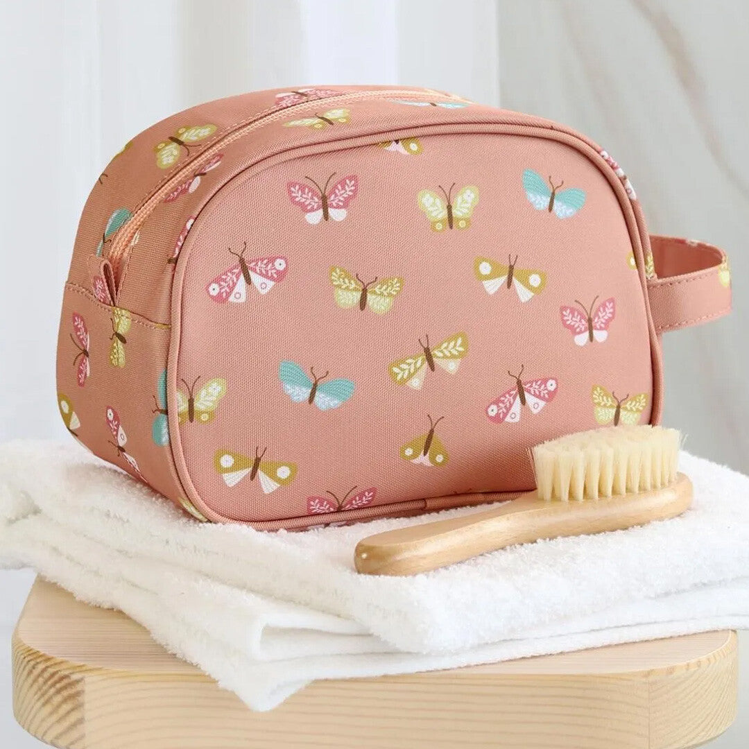 Roze toilettas met vlinders op witte handdoeken naast een houten babyborstel.