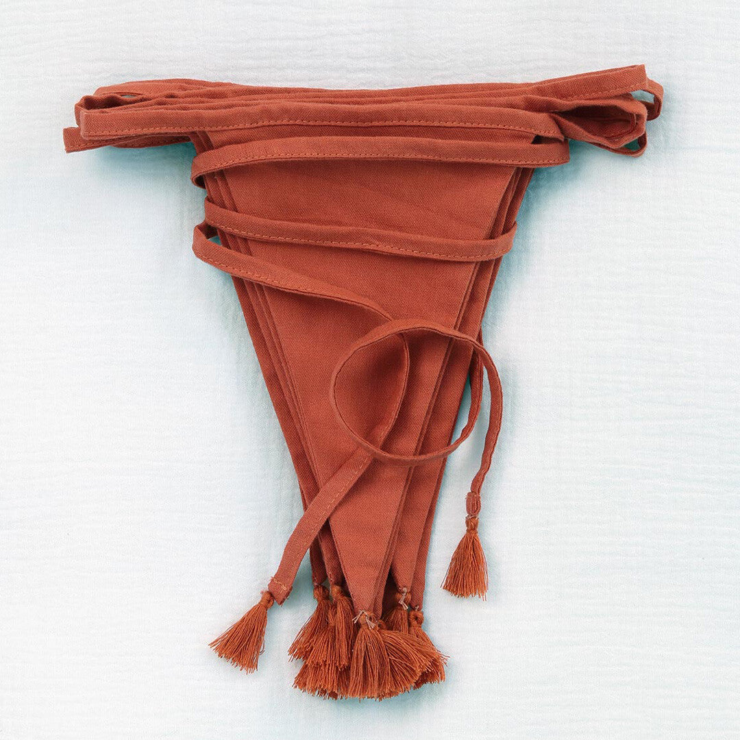 Een opgevouwen a little lovely company terracotta stoffen vlaggenslinger met kwastjes, van bovenaf gezien.