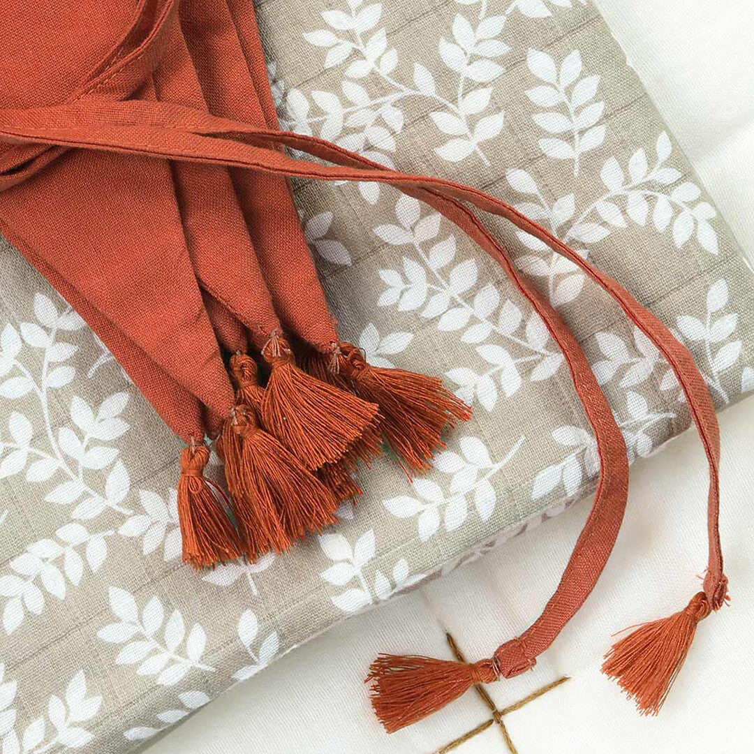 Detail van de a little lovely company terracotta stoffen vlaggenslinger met kwastjes en strikken op een grijs-wit doek.