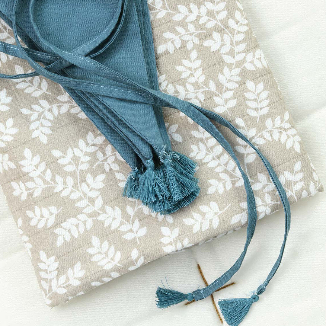 a little lovely company stoffen slinger in vintage blauw, opgevouwen op een beige doek met wit bladpatroon.
