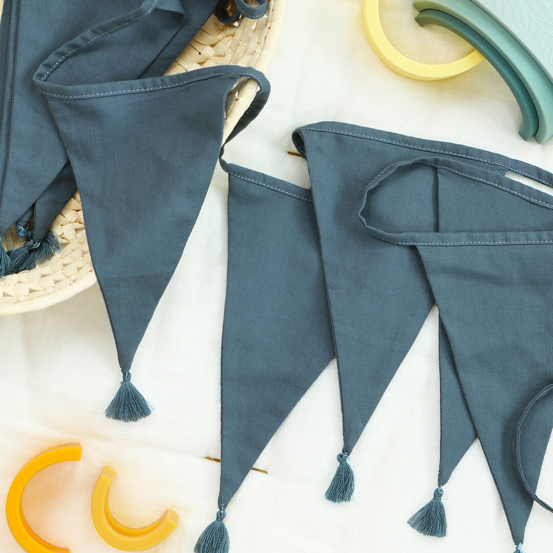 a little lovely company stoffen slinger in vintage blauw, hangend met speelgoed op de achtergrond.