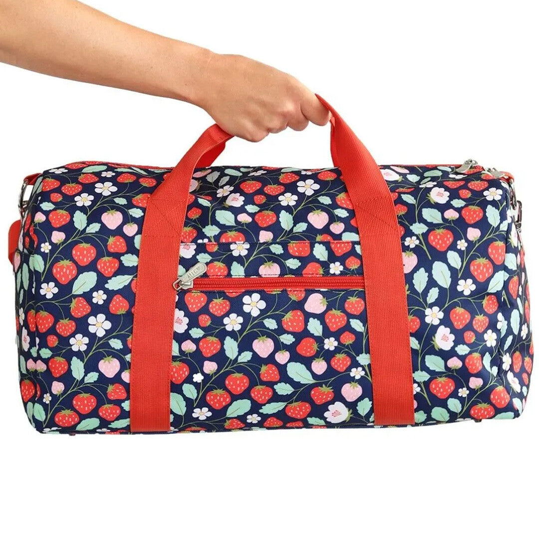 Een hand houdt de a little lovely company kinder weekendtas met aardbeienprint vast.