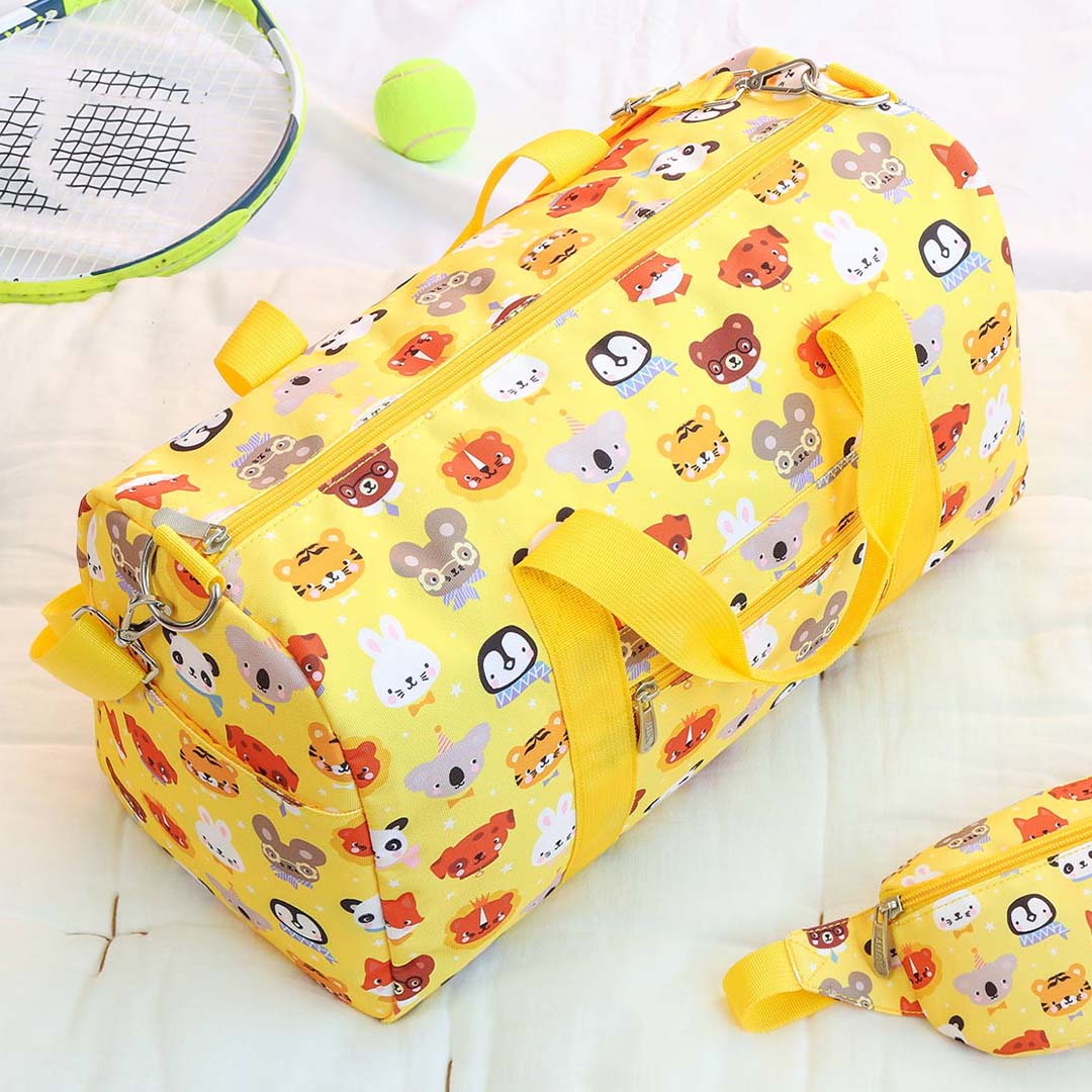 De gele kinder weekendtas met dierenvriendenpatroon ligt op een bed naast een tennisracket en een bijpassend heuptasje.