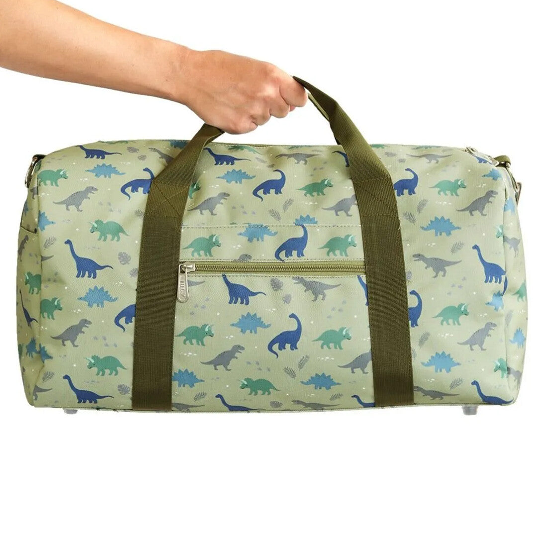 Een hand houdt de a little lovely company groene kinderweekendtas met dinosauruspatroon vast.