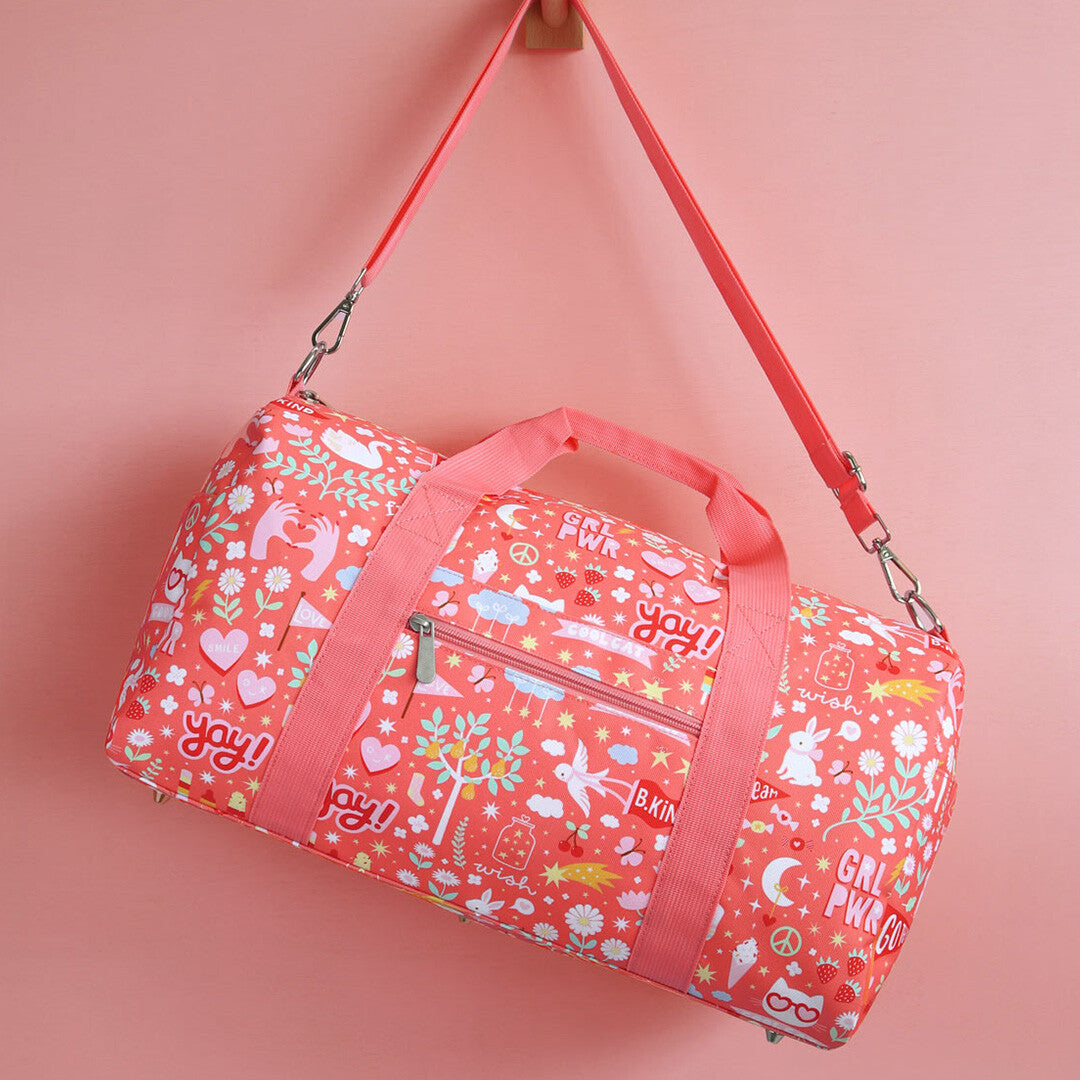 a little lovely company roze weekendtas voor kinderen met vrolijke print, hangend aan een haak tegen een roze achtergrond.