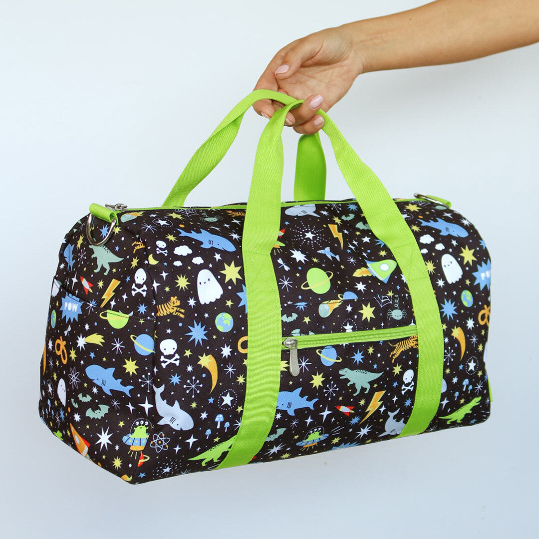 Een hand houdt de a little lovely company kinder weekendtas met galaxy patroon en groene hengsels vast.