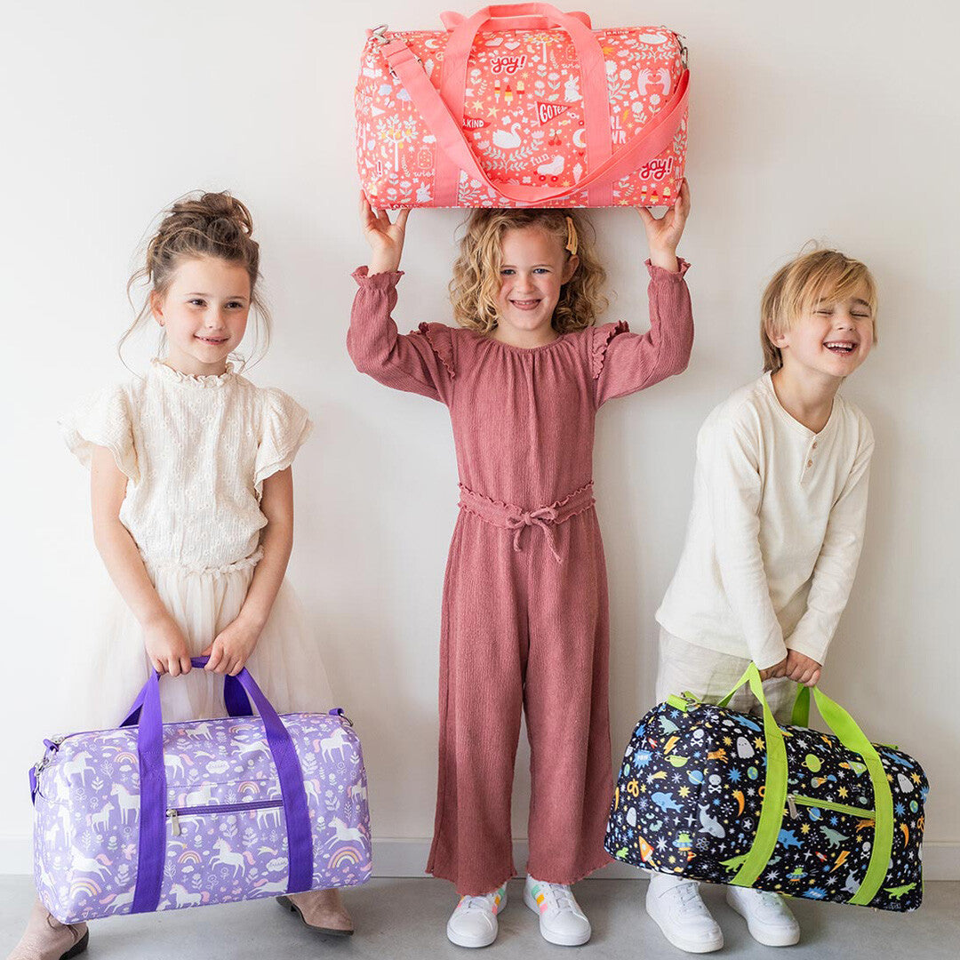 Drie lachende kinderen poseren met verschillende a little lovely company kinder weekendtassen, waaronder de galaxy tas.
