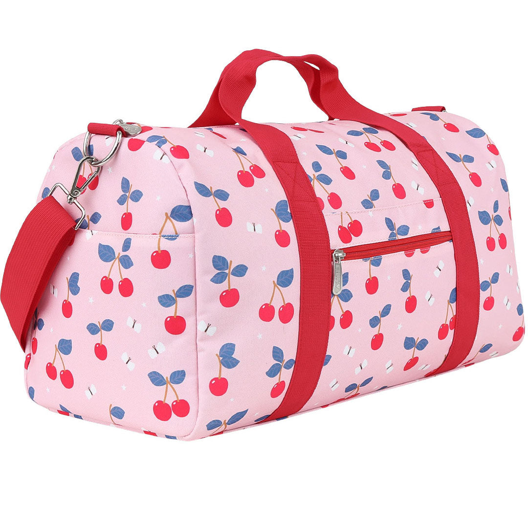 Een roze a little lovely company kinder weekendtas met kersenprint en rode hengsels, schuin gefotografeerd op een witte achtergrond.