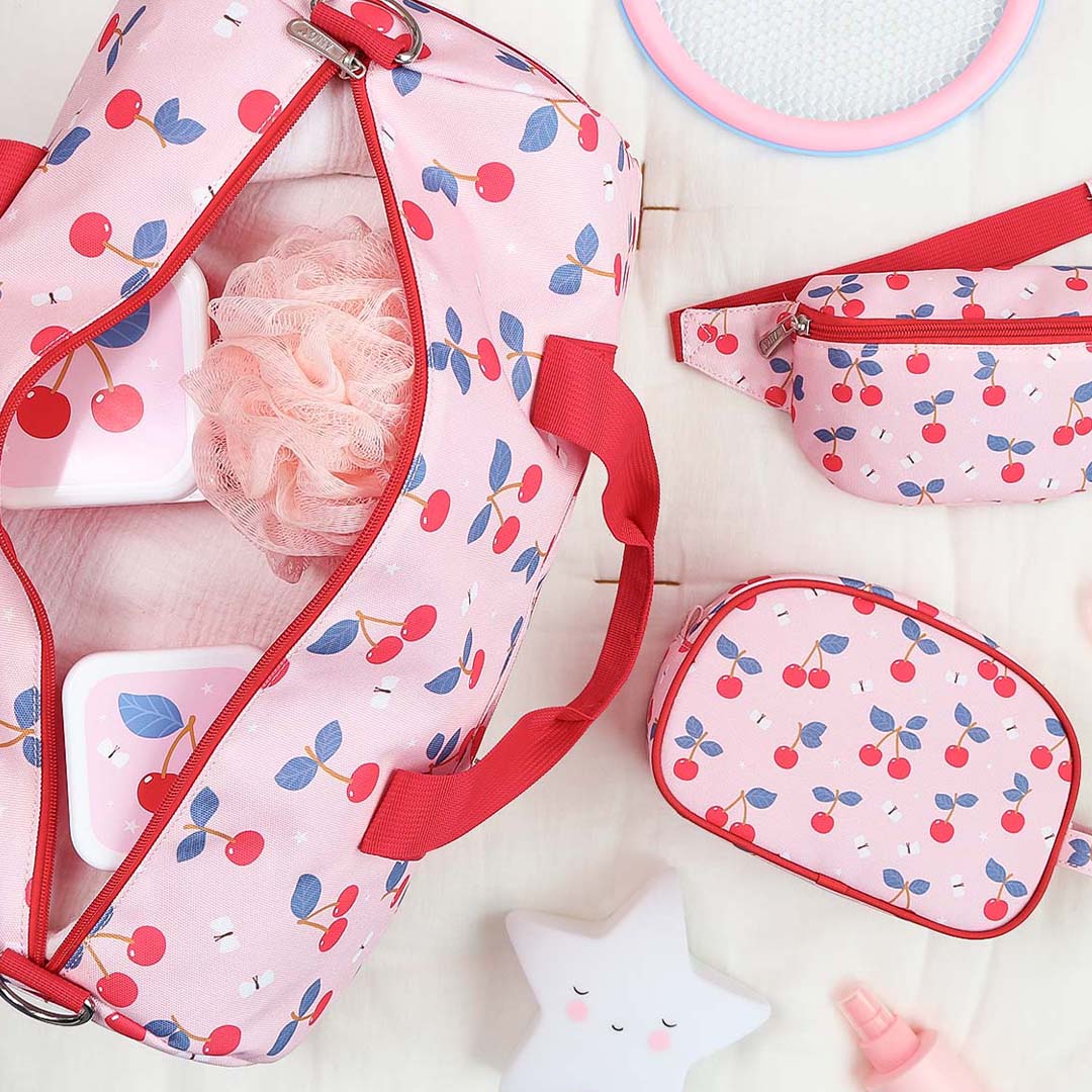 Een open roze a little lovely company kinder weekendtas met kersenprint toont de inhoud, naast een bijpassende heuptas en toilettas.