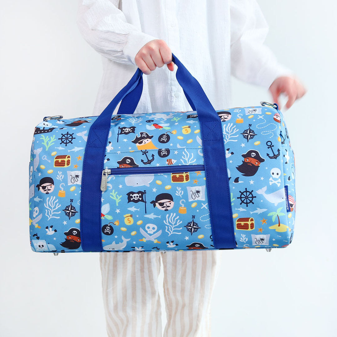 Een persoon houdt de a little lovely company kinderweekendtas met piratenthema vast aan de handvatten.