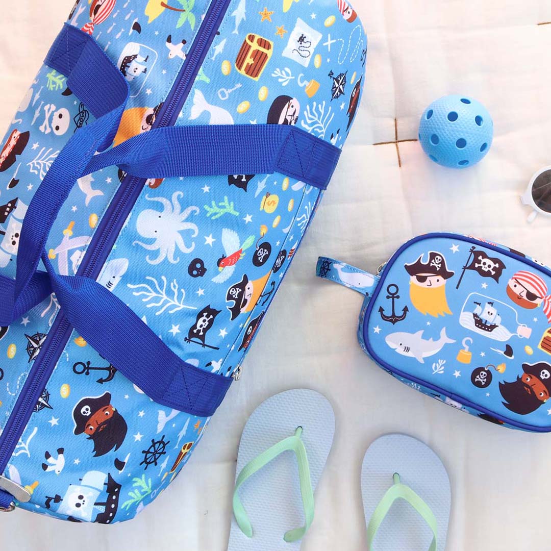 De a little lovely company kinderweekendtas en toilettas met piratenthema liggen op een deken met strandaccessoires.