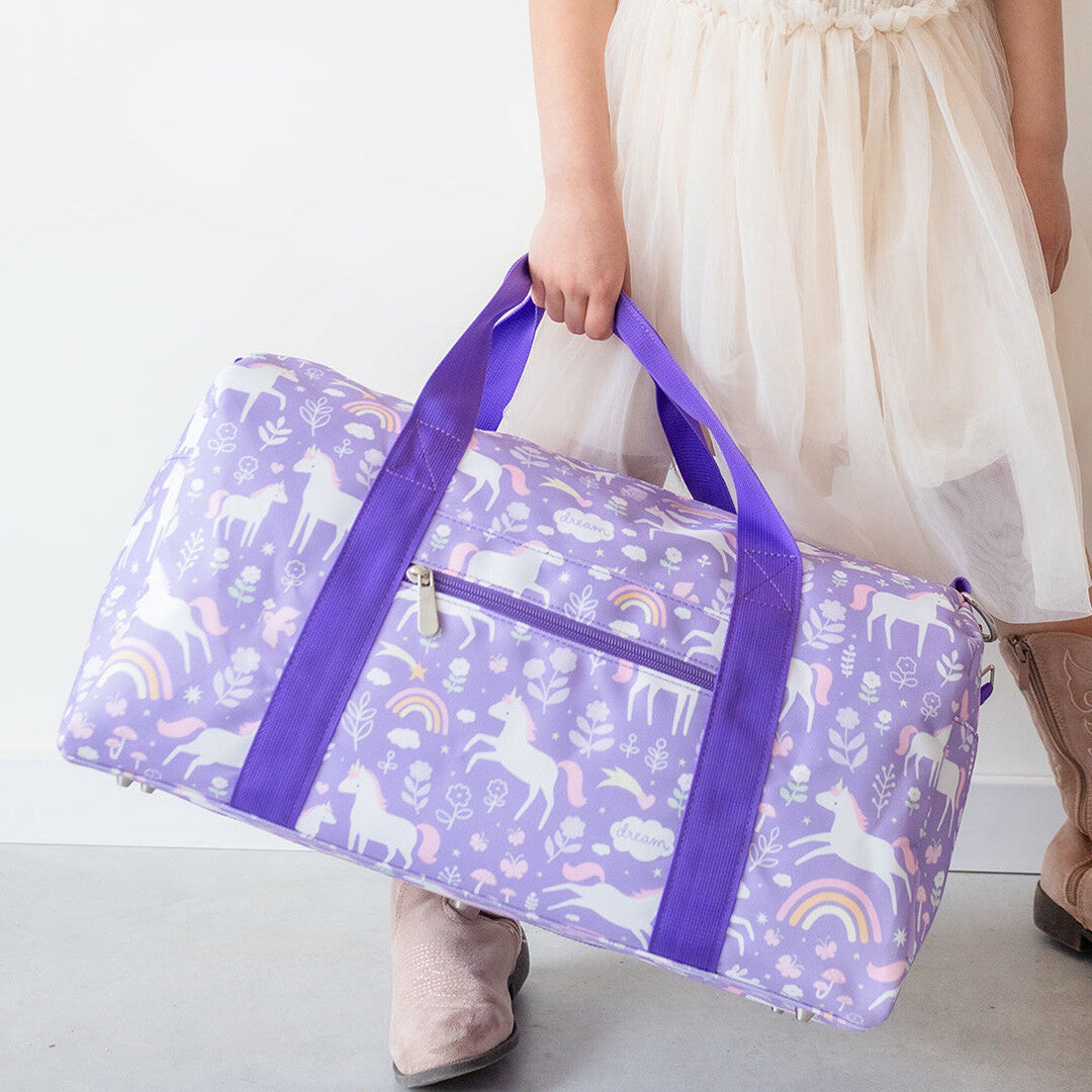 Kind draagt de a little lovely company paarse weekendtas met eenhoornpatroon, schuin van voren.