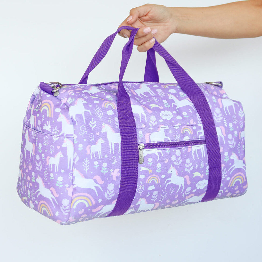 Een hand houdt de a little lovely company paarse weekendtas met eenhoornpatroon vast, schuin van voren.
