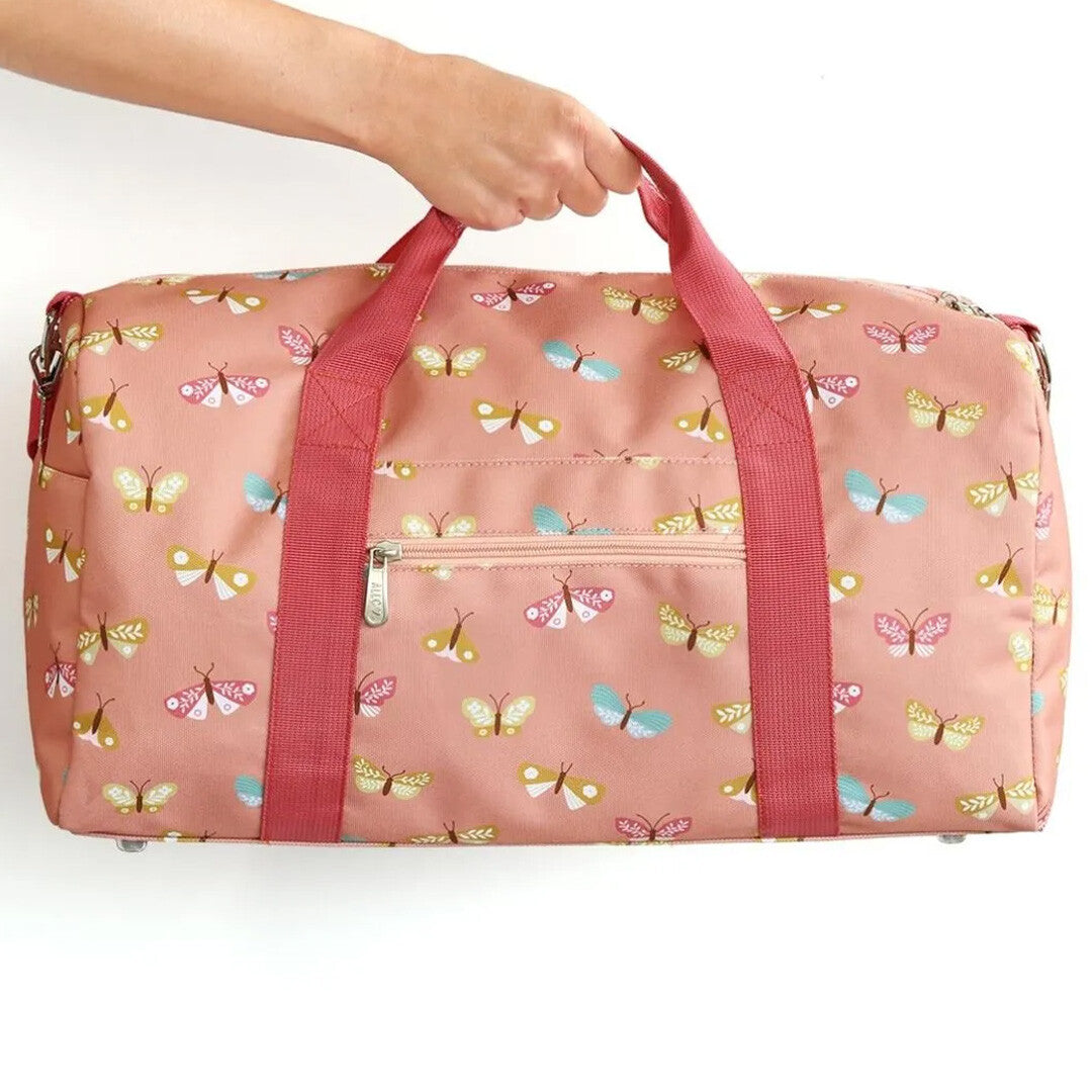 Een hand houdt de a little lovely company roze kinderweekendtas met vlinderpatroon vast.