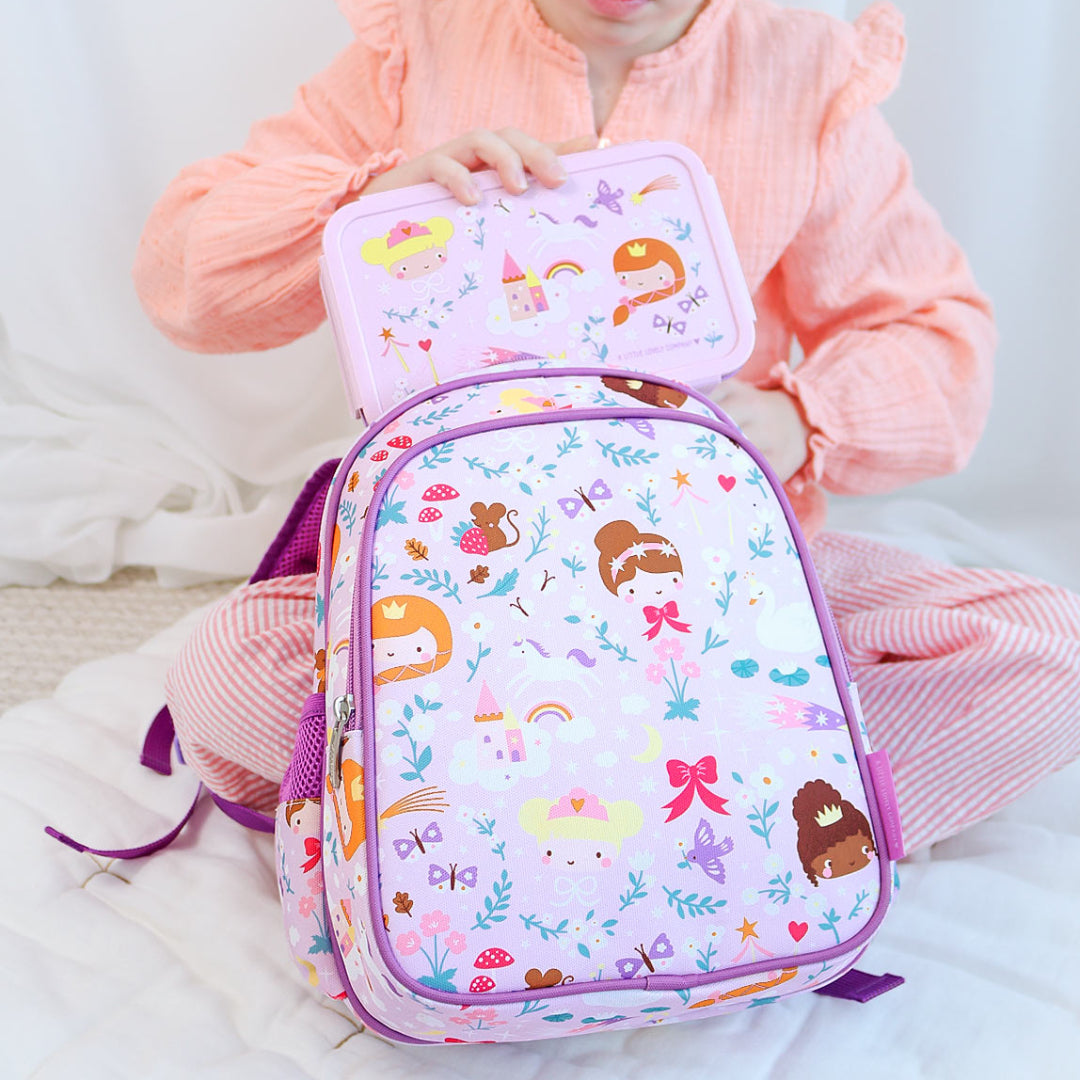 Een kind houdt de a little lovely company bento broodtrommel met prinsessenpatroon vast, met een bijpassende rugzak ervoor.