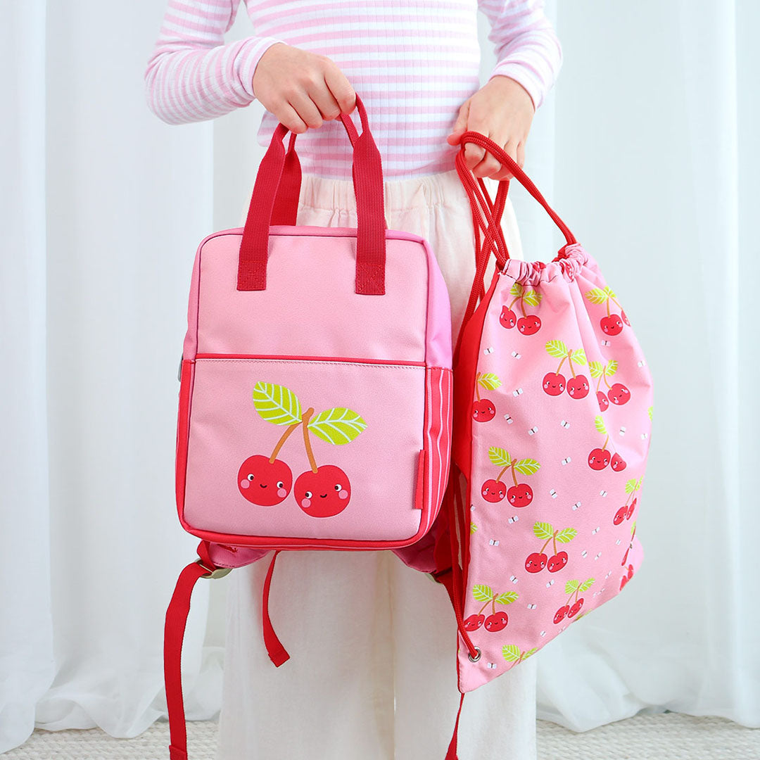 Kind toont de A Little Lovely Company roze gymtas en bijpassende rugzak met kersjes.