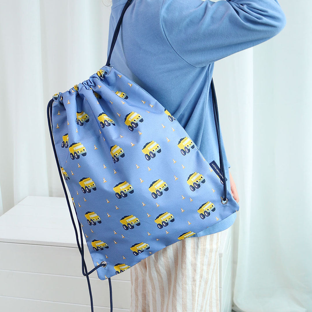 Een persoon draagt de blauwe a little lovely company gymtas met kiepwagenpatroon over de schouder.