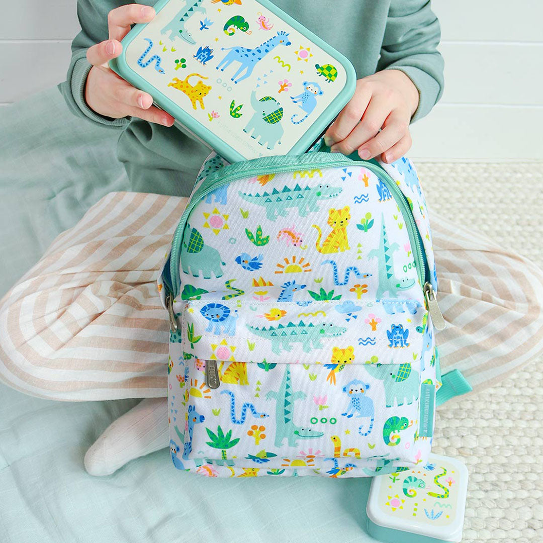 Een kind stopt een lunchbox in de open a little lovely company kleuterrugzak met jungle dierenprint.