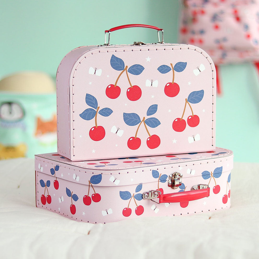 Twee roze a little lovely company kinderkoffers met kersenpatroon, op elkaar gestapeld in een kinderkamer.