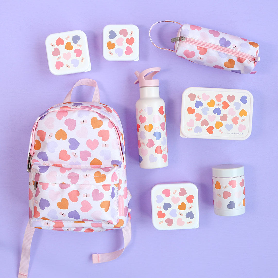 Een collectie A little lovely company kinderartikelen met hartjespatroon, waaronder een rugzak, drinkfles en lunchboxen, op een paarse achtergrond.