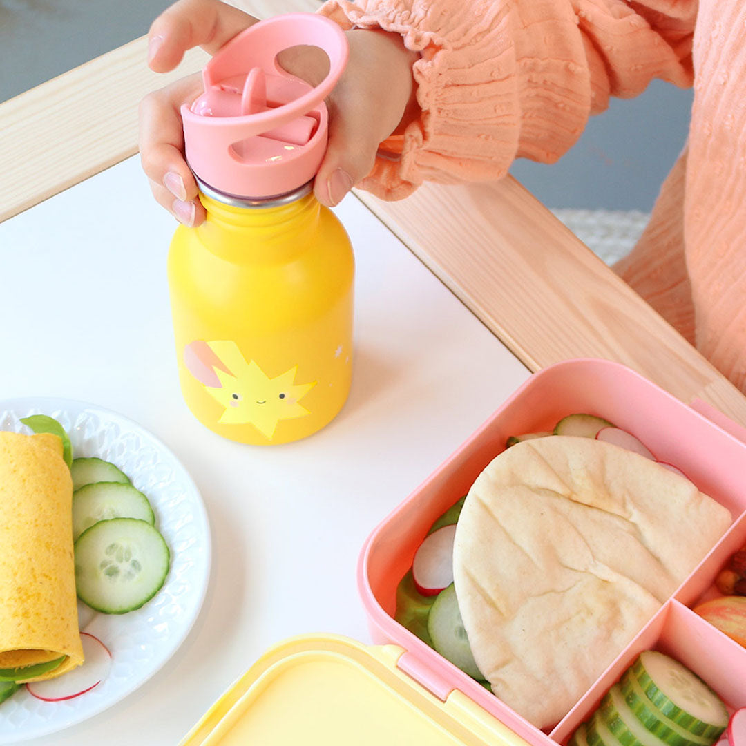 De gele kinder drinkfles met vallende ster design staat op tafel naast een lunchbox.