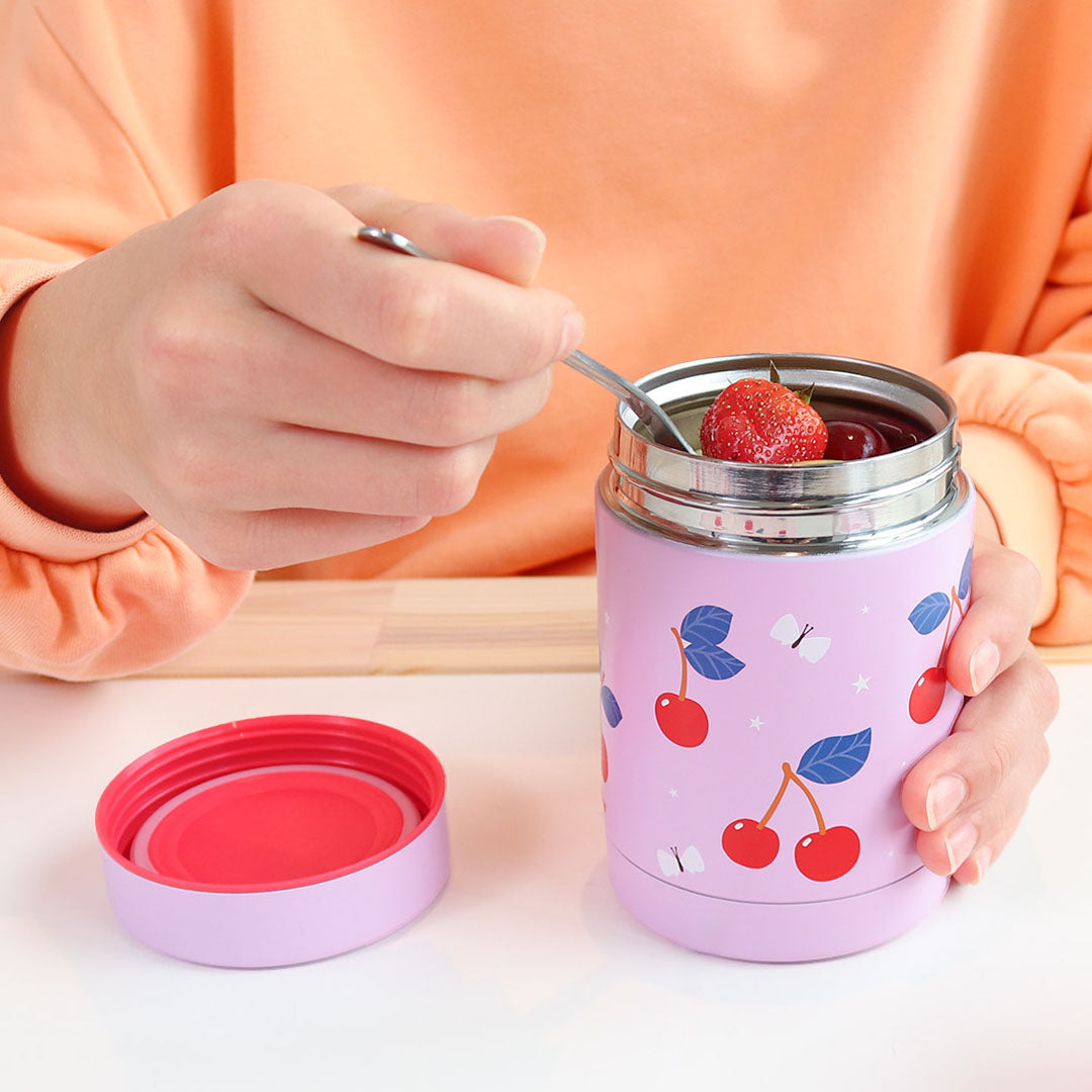 Een persoon eet met een lepel uit de open A Little Lovely Company roze thermos voedselpot met kersenpatroon.