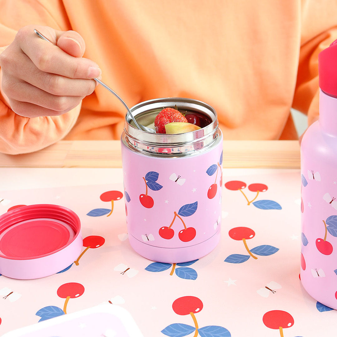 Een persoon eet uit de open A Little Lovely Company roze thermos voedselpot met kersenpatroon, naast een bijpassende drinkfles.