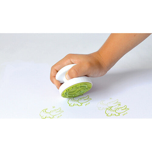 Een kinderhand drukt een Aladine Stampo Baby stempel met een krokodil af op wit papier.