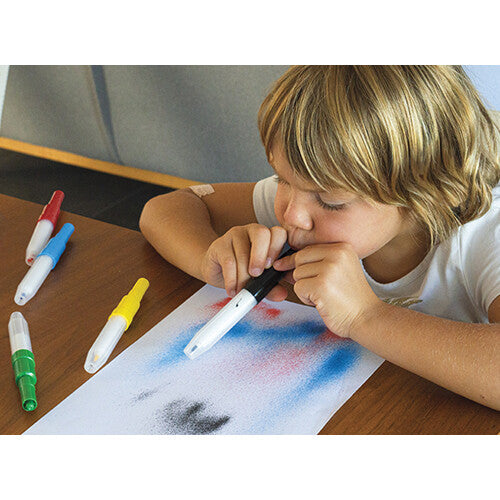 Een kind blaast met een Aladine textiel blaasstift kleur op papier, met andere stiften ernaast.