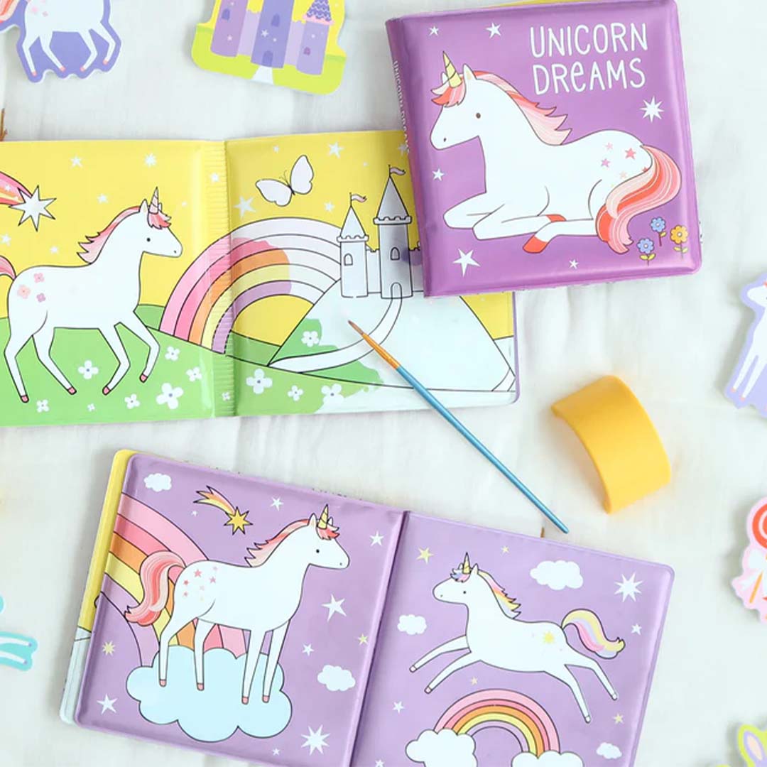 Drie open en gesloten magische badboekjes met eenhoorns, regenbogen en kastelen, samen met een kwastje en sponsje.