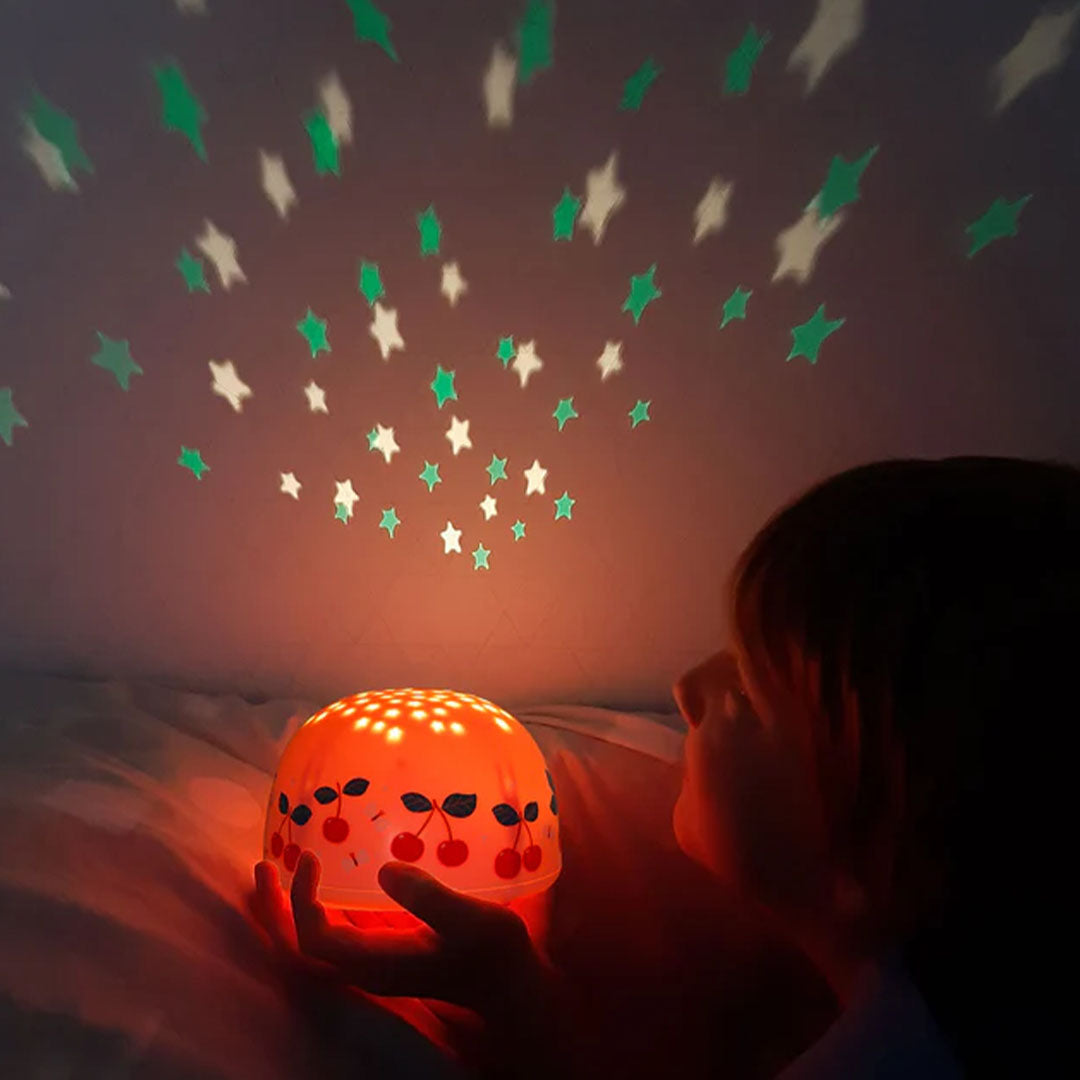 Een kind kijkt naar de A Little Lovely Company nachtlamp en sterprojector die sterren op de muur projecteert.